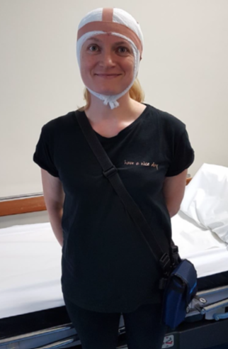 A patient stood by a bed side, wearing a head bandage.