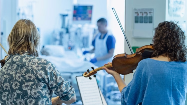 two musicians play to a patient on an ICU ward.