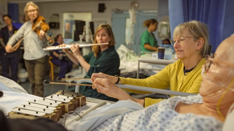 A patient and family member play along to live music on an ICU ward.