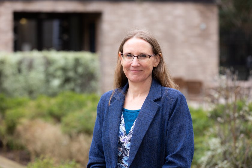 A woman with long brown hair and glasses, smiling for the camera.