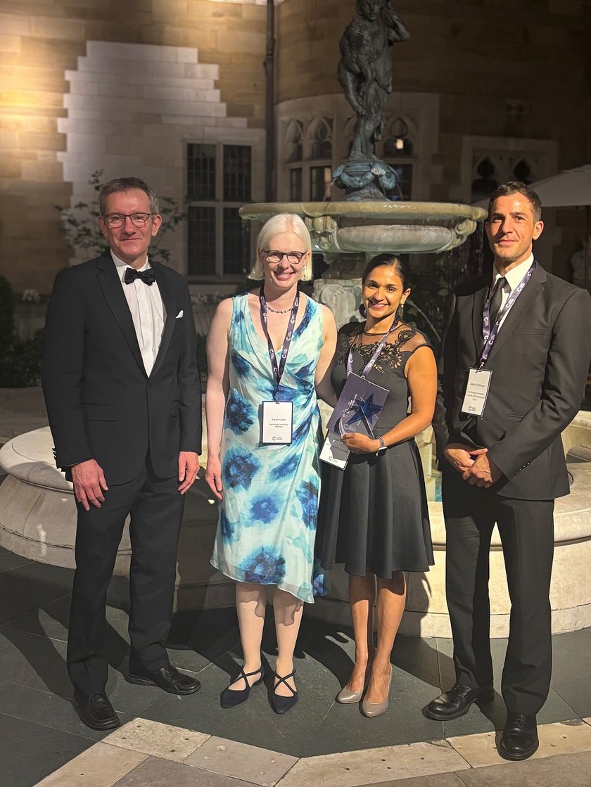 A group photo of four people who won the award next to a fountain