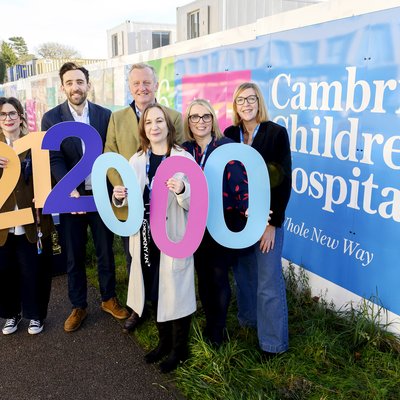 People standing outside Cambridge Children's Hospital hoardings holding £212,000 in colourful printed letters