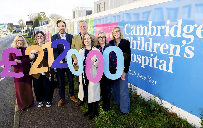 People standing outside Cambridge Children's Hospital hoardings holding £212,000 in colourful printed letters