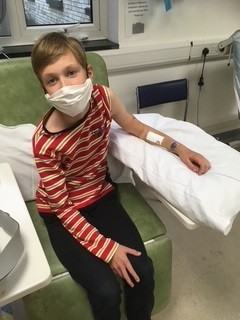 A boy in a clinical room waiting to have his arm looked at following an operation. He looks quite happy, despite wearing a mask