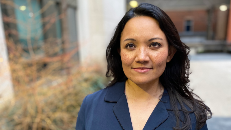 Dr Basu in a blue blouse looking into the camera with plants and buildings in the background