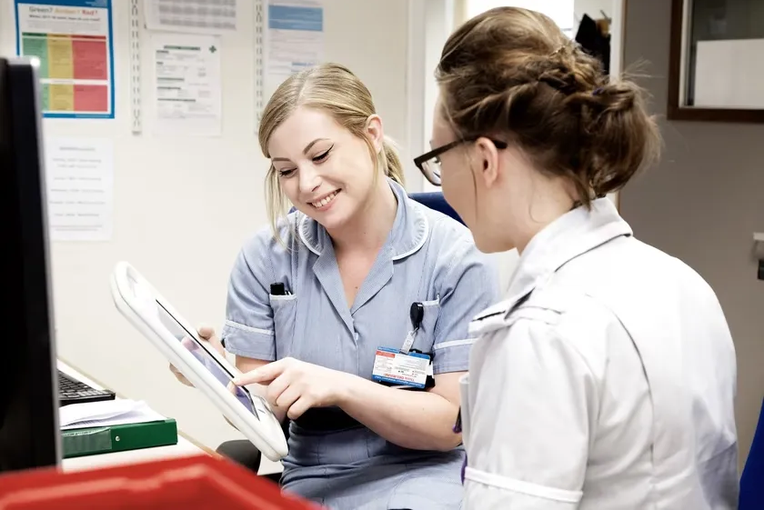 Two nurses looking at a tablet device with one pointing at the screen