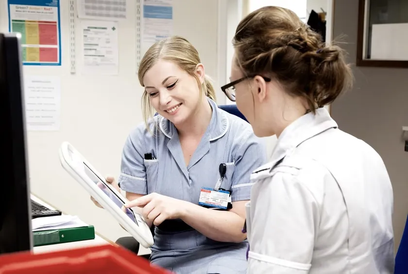 Two nurses looking at a tablet device with one pointing at the screen