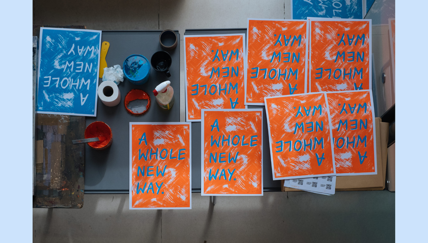 A set of freshly made colourful prints in blue and orange with the words A Whole New Way on them. these were posters made by delegates