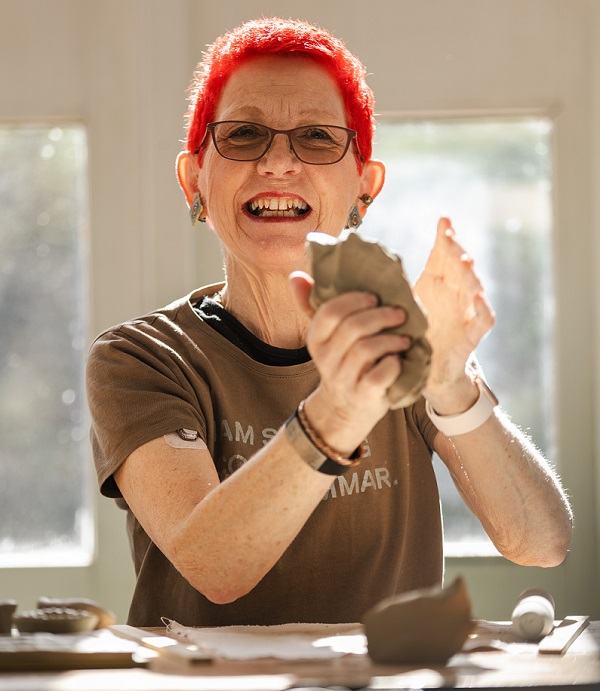 A lady with short red hair holding some clay in a studio