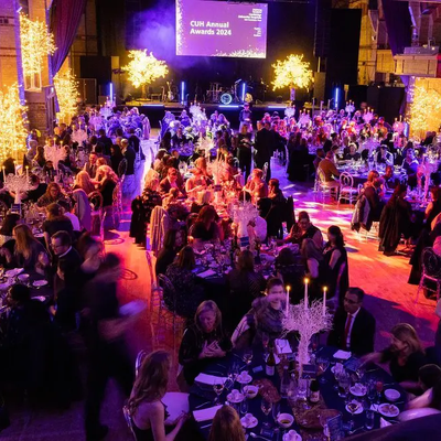 A vibrant event hall decorated with glowing trees and elegant lighting, filled with guests seated at round tables for the CUH Annual Awards 2024. The atmosphere is lively and celebratory.