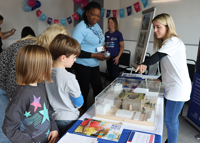 Two children looking at a hospital model and a woman pointing at it