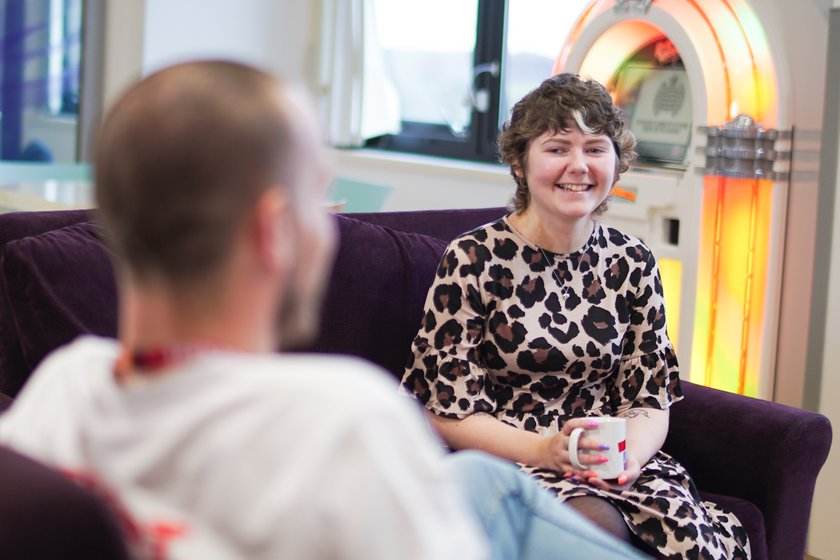 A Teenage Cancer Trust Youth Support Coordinator sitting on a sofa in the teenage cancer trust unit holding a mug