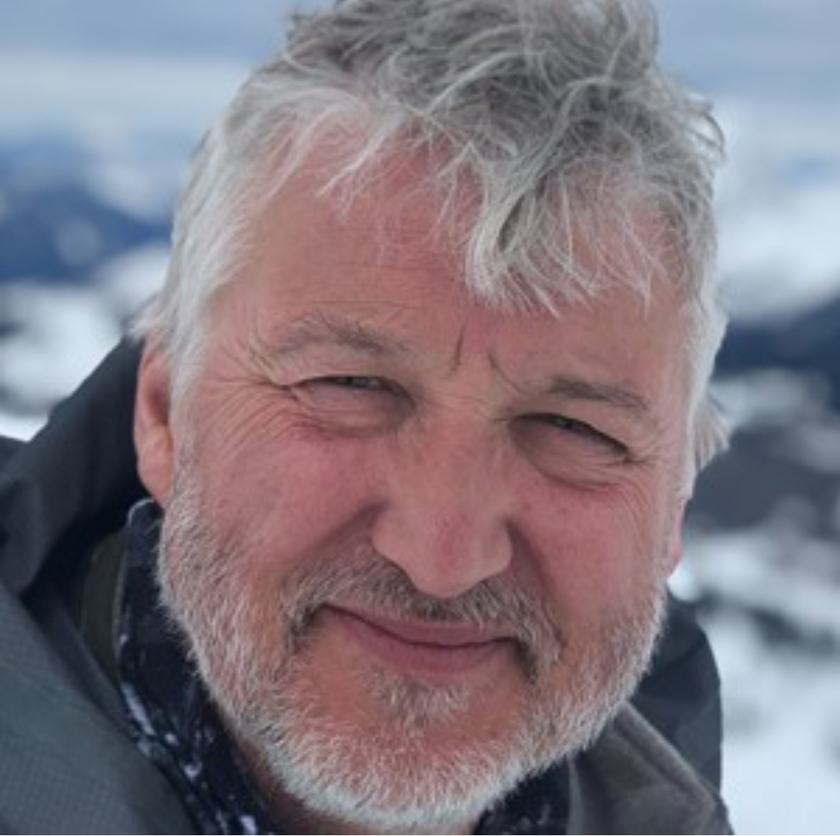 A headshot of a man with grey ruffled hair and short grey/white beard