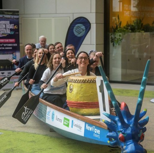A team of women and men sitting in a Dragon Boat holding paddle oars