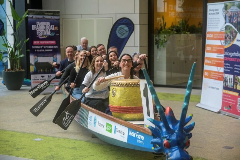 A team of women and men sitting in a Dragon Boat holding paddle oars