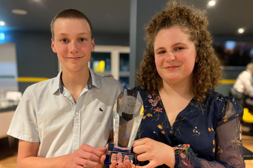 A boy with short fair hair and a smart white shirt with a teenager girl with curly hair and a pretty black and white patterned dress holding a glass award saying Inspirational Youth Stars
