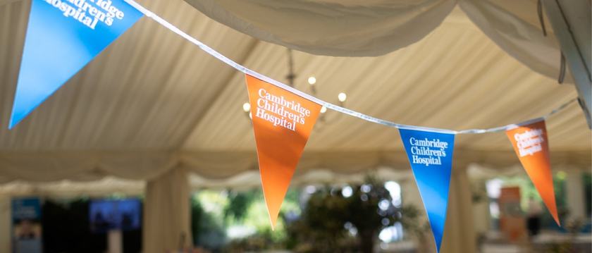 orange and blue bunting hanging from a marquee in the sunshine. The Cambridge Children's Hospital logo is on each one