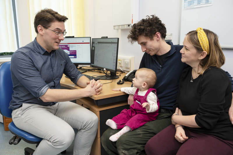 Dr Emile Hendriks meeting with Safi and her parents in a consultation room. Safi is sat on her dads lap and looking intently at Dr Hendriks.