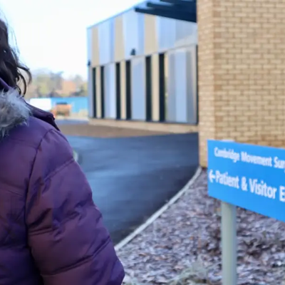 Person walking towards the patient and visitor entrance sign for Cambridge Movement Surgical Hub.