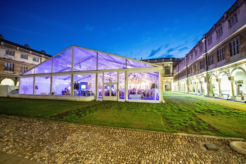 A huge clear sided marquee on a grass quadrangle surrounded by old buildings