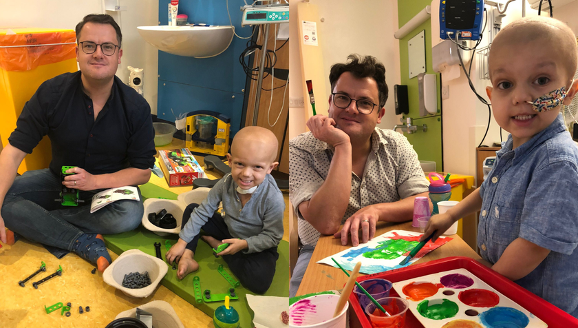 A man with brown hair and glasses playing with his young son, who has cancer, in hospital. They are painting together and also playing a building game