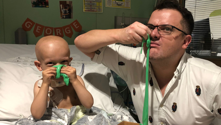 A little boy who has cancer and is in a hospital bed, with his dad holding green slime up to their noses and pretending it's giant bogeys