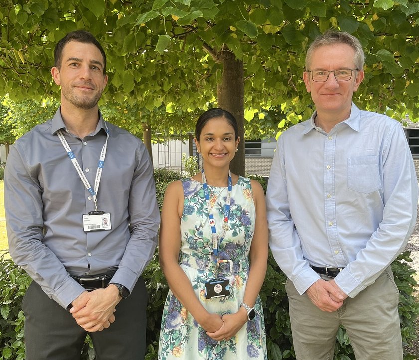 A group photo of two men and a woman standing outside near some trees