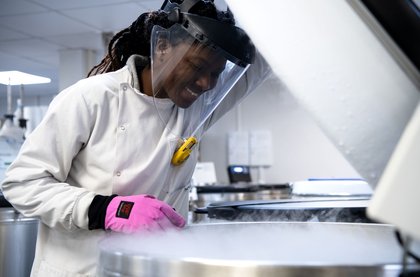 Woman in white lab coat with pink glove looking down and smiling
