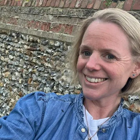 Hannah Threlfall, a blonde woman wearing a denim jacket smiling into the camera in front of a large stone wall