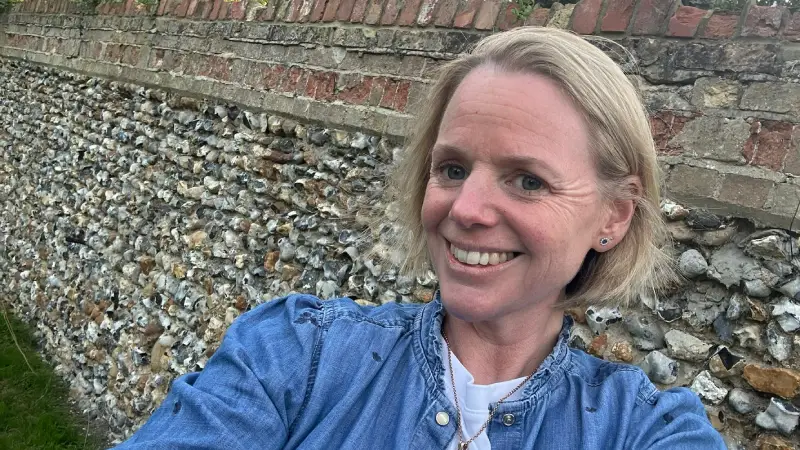 Hannah Threlfall, a blonde woman wearing a denim jacket smiling into the camera in front of a large stone wall