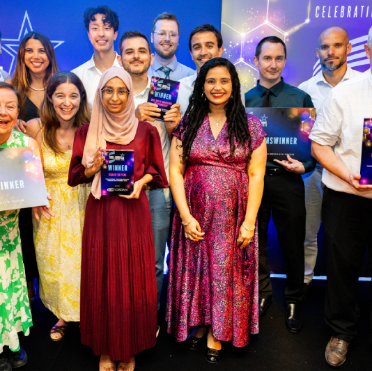 A large group of people holding award certificates standing in front of a coloured backdrop