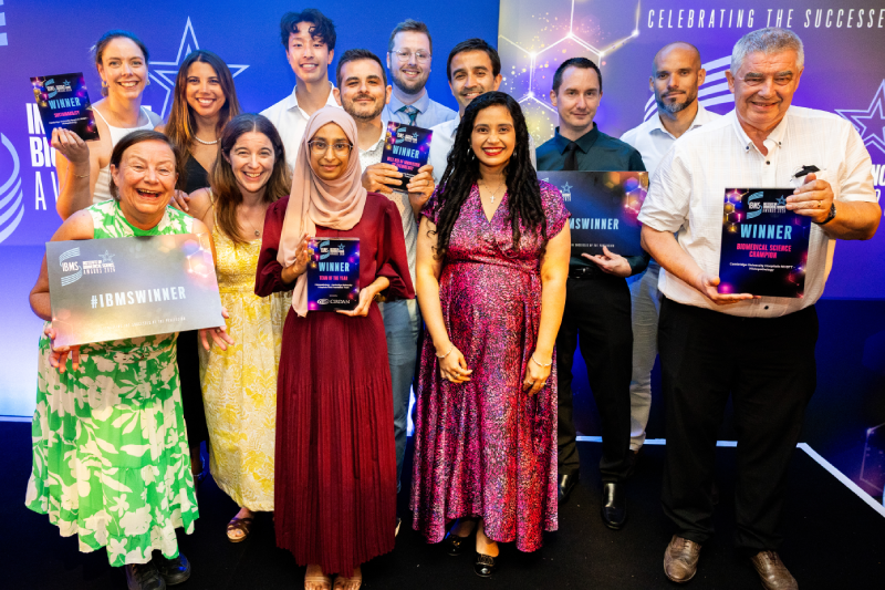 A large group of people holding award certificates standing in front of a coloured backdrop
