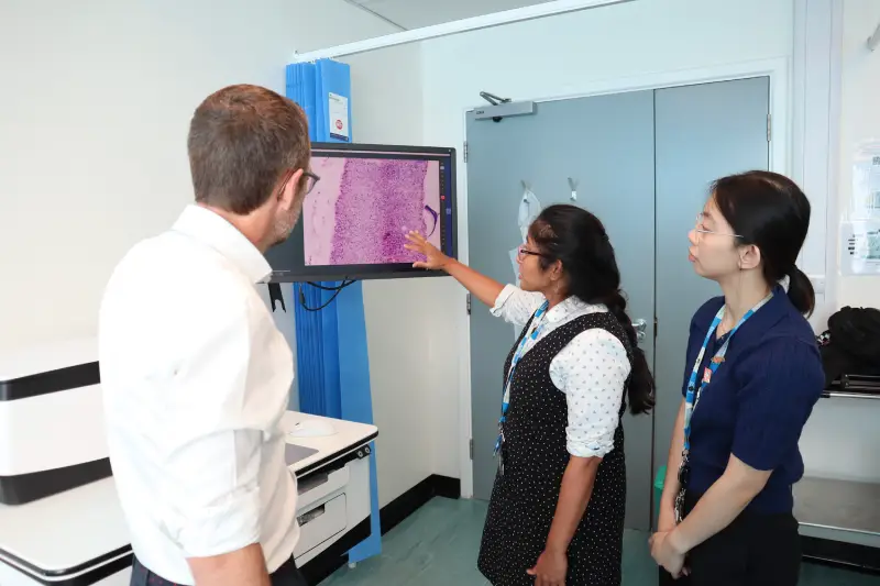 Grant Stewart and two female colleagues facing away from the camera towards a screen showing images from the confocal microscope shown in the back left of the image.