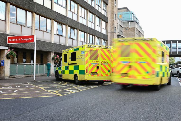 Ambulances driving towards hospital. A red accident and emergency sign can be seen to the left of the ambulances..