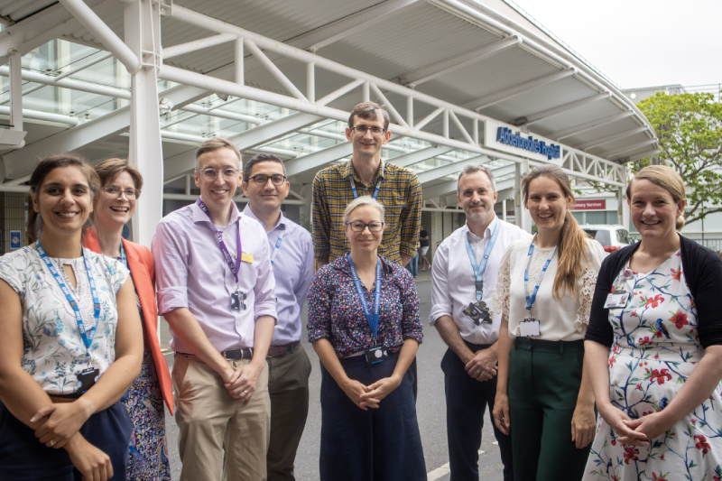 Nine people standing together facing the camera outside the main entrance of Addenbrooke's Hospital.