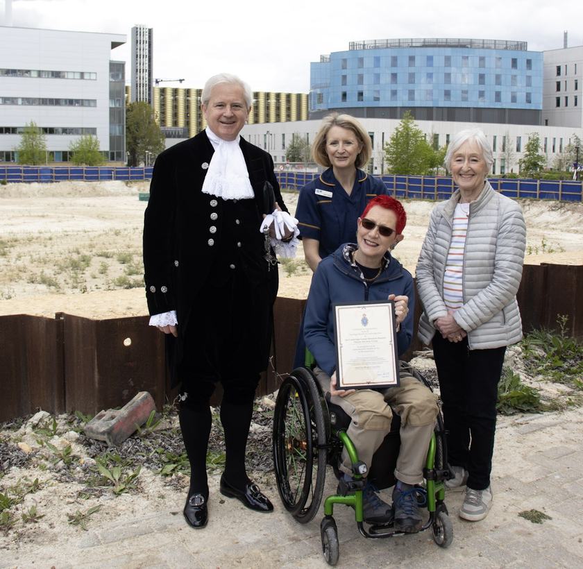 A man wearing a black outfit presenting a group of people a certificate opposite a building site