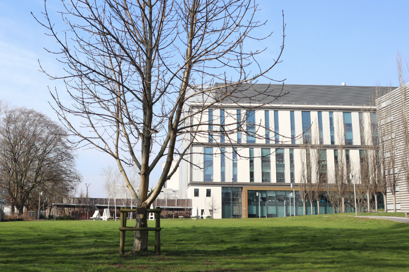 A large modern research building sitting behind a green space with trees