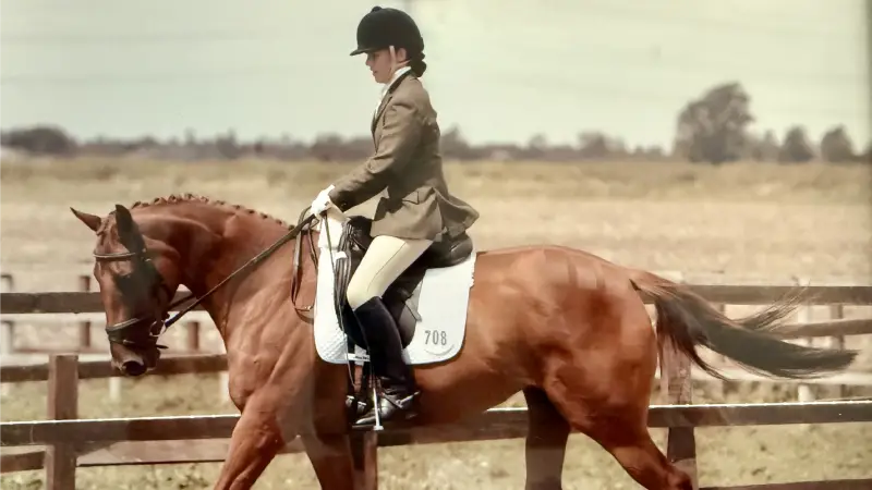 Isobel in riding gear on a chestnut horse facing to the left of the image with fields and fences in the background.