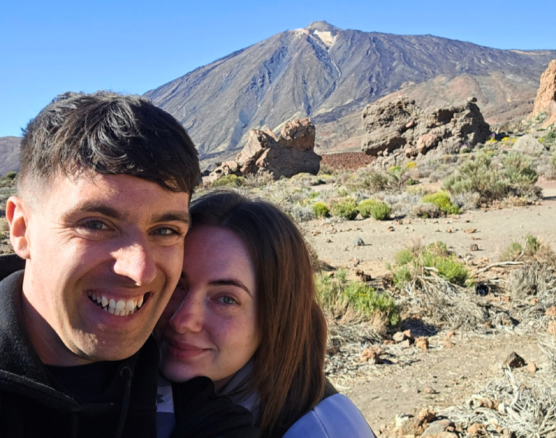 A selfie of Jack and Chloe in front of a volcanic landscape and blue sky