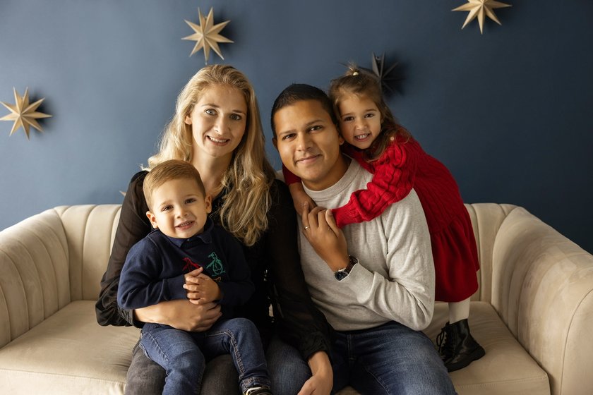 Jacob's family sitting on a cream sofa in front of a dark blue wall with stars on it. Jacob's mum is sat on the left with Jacob on her knee. Jacob's dad is sat on the right and Jacob's sister is standing on the sofa with her arms around dad's shoulders.