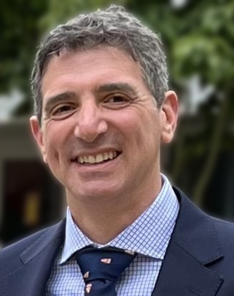 Professor James Nathan wearing a dark suit and college tie outside with a tree in the background