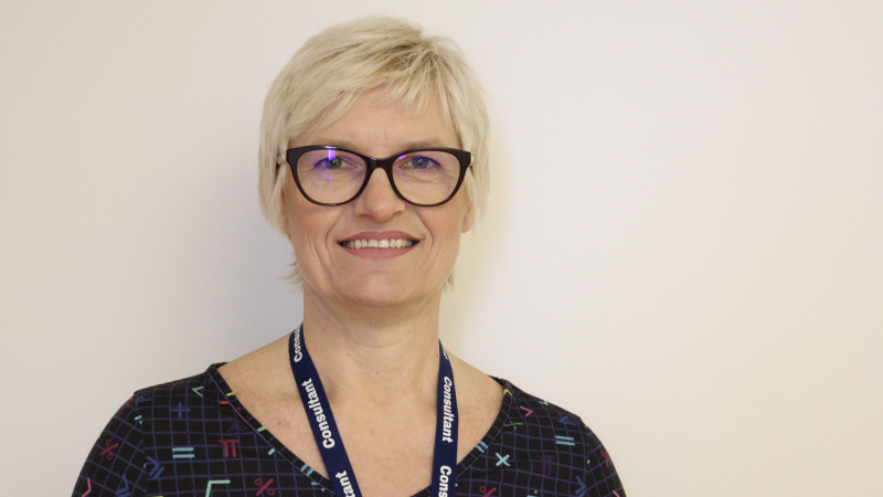 Dr Gajweska-Knapik smiling into the camera wearing a dark coloured dress with mathematical symbols on it standing in front of a blank wall