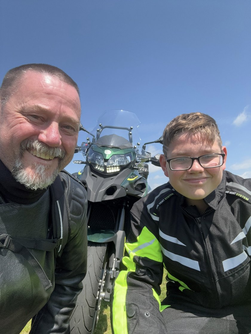 Two men wearing motorcycle clothing with a motorbike in the background