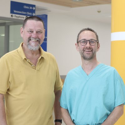 Two men in a hospital, one man wearing medical scrubs and another wearing a green polo shirt