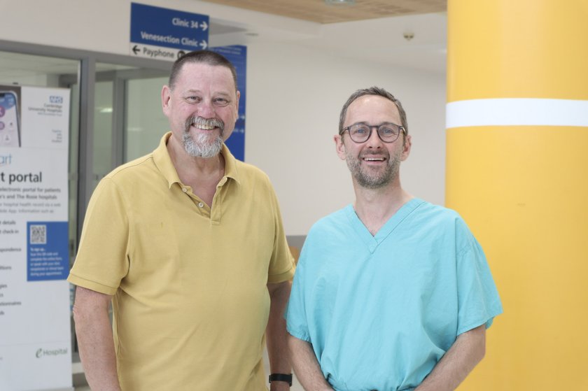Two men in a hospital, one man wearing medical scrubs and another wearing a green polo shirt