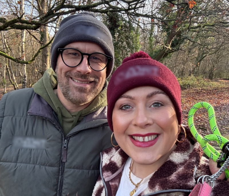 Laura and Matt standing together in a wood wearing beanie hats and thick coats.