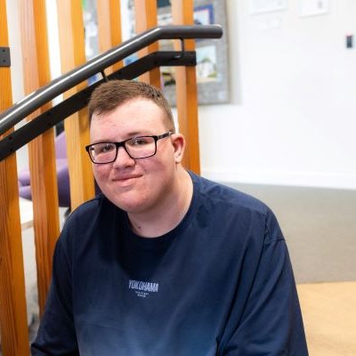 A teenager wearing glasses smiling and sitting on a staircase.