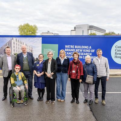 Patients and staff involved in the Cambridge Cancer Research Hospital programme are pictured standing in front of the the newly designed site hoardings. The hoardings are bright and an artist impression of the future hospital can be seen on them