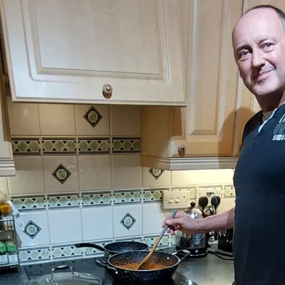 Mark in a black t-shirt cooking on a hob in a kitchen.