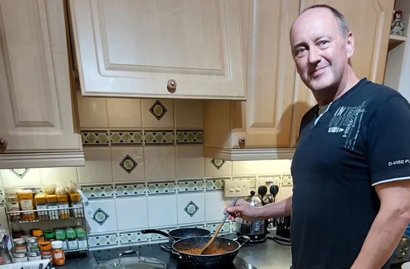 Mark in a black t-shirt cooking on a hob in a kitchen.